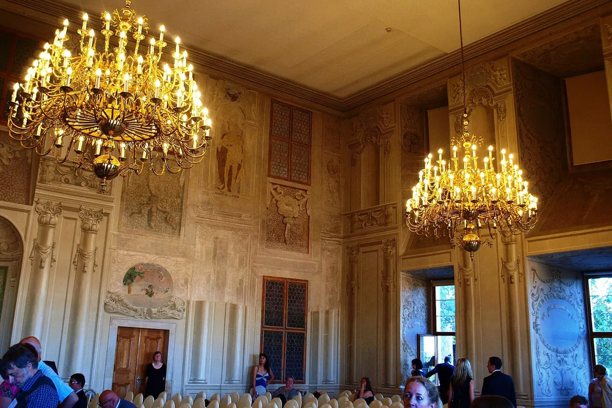 Ein Saal des Palastes mit vergoldeten Kronleuchtern, bemalten Wänden und einem Fenster ins Grüne.