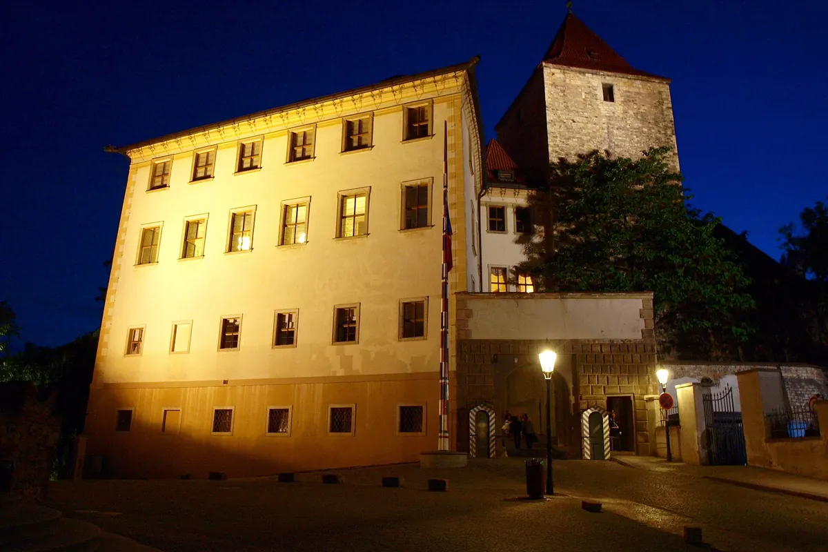 Der Lobkowicz-Palast bei Nacht auf dem Burgberg, mit einer Straßenlaterne und einem Turm dahinter.