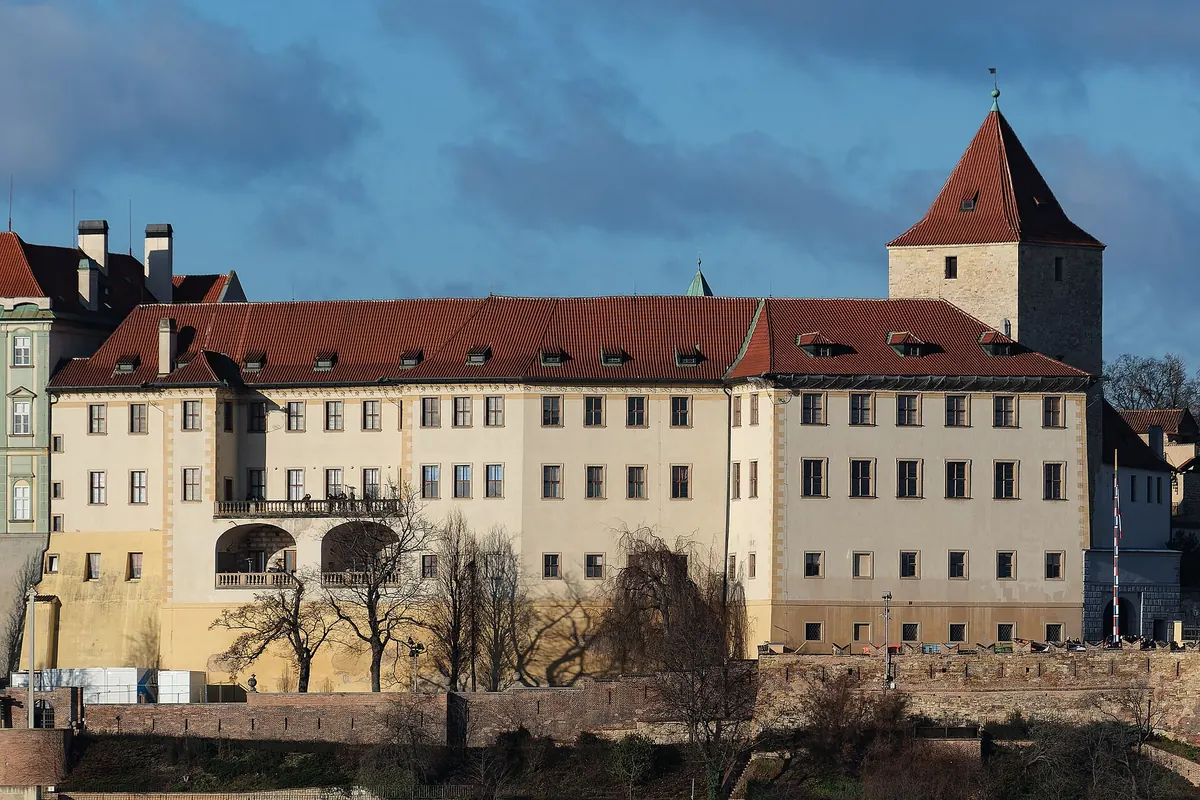 Der Lobkowicz-Palast und der dunkle Turm daneben auf dem Burgberg, bei tiefer Sonne von jenseits des Flusses gesehen.